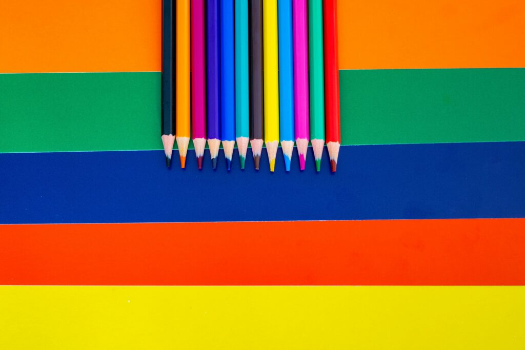 A collection of colored pencils arranged on a bright striped background, showcasing vivid rainbow hues.